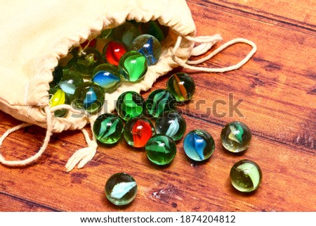 Colourful glass marbles and a cloth bag on a wooden background