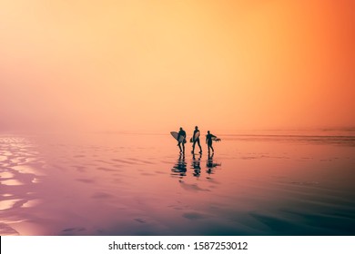  Colourful image. Early morning, surfers walking on the beach. Three surfers, walk along an ocean beach with their surfboards in hand.