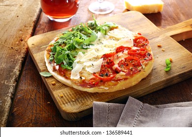 Colourful Italian pizza in the national colours topped with fresh green rocket leaves, white shavings of cheese and red tomatoes in three stripes standing on a wooden board on an old rustic table