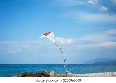 Colourful Kite Flying In Blue Sky With The Sea And Mountains In The Background