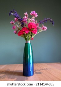 Farbige, rosa und violette, frische Blütenanordnung in einer bunten Vase mit egellblauem Hintergrund - Pelargonien. – Stockfoto