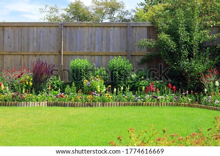 Colourful Pretty Flower And Shrub Border Surrounded By A Fence And A Green Lawn In A Home Back Garden.