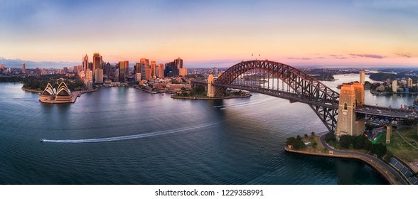 Colourful sky over Sydney city CBD high-rise towers at sunrise around Sydney harbour and the Sydney Harbour bridge in elevated aerial panorama.