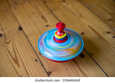 A Colourful Spinning Top On A Wooden Floor Spins Round Very Fast So As To Create Motion Blur. The Red, Yellow And Blue Colours Blend Together To Create A Watery Appearance. 