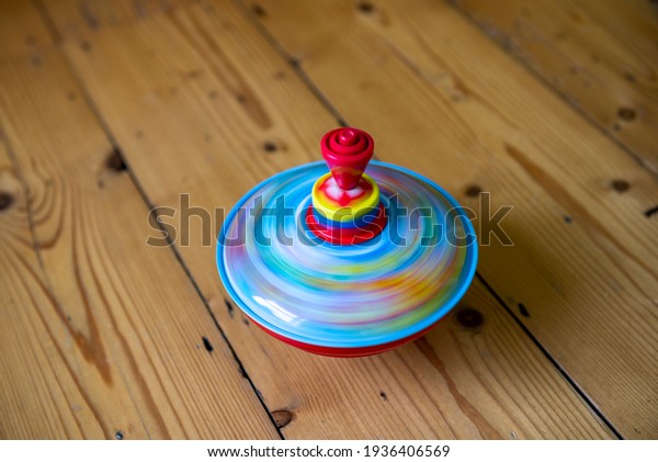 A colourful\
spinning top on a wooden floor spins round very fast so as to\
create motion blur. The red, yellow and blue colours blend together\
to create a watery appearance.\
