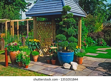 A Colourful Urban Garden With Planted Containers Of Flowers And A Cloud Pruned Topiary Tree With Covered Seating Area