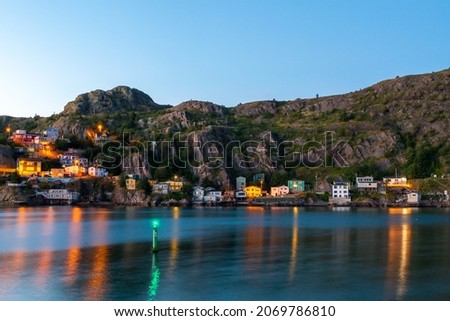 Colourful wooden historic houses built on a hillside, Signal Hill, in St. John's, Newfoundland. The hill overlooks the harbour and colorful lights from the homes are reflecting on the calm water. 