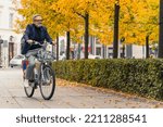 Colours of autumn. 60-year-old happy gray-haired man cycling on pavement at his favorite city park. Active leisure time in nature. High quality photo