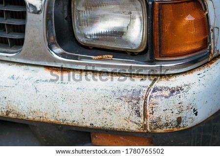 Colse up to decay and rust on the front bumper of an old white truck. Rust hole on old worn painted metal surface.