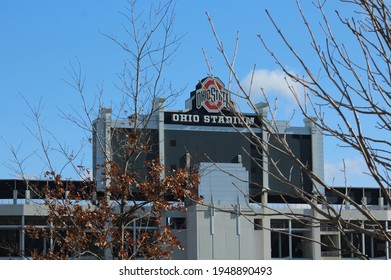 Columbus OH: USA: April 1, 2021 – Ohio State University Football Stadium Sign And Logo. Blue Sky. Bare Tree Branches In Foreground. 