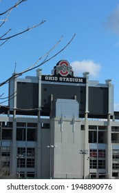 Columbus OH: USA: April 1, 2021 – Ohio State University Football Stadium Sign And Logo. Blue Sky. Bare Tree Branches In Foreground.