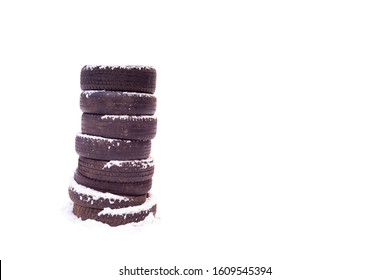 A column of old black car tires under white snow. Car tires are stacked vertically on top of each other on a white background. Isolated photo of the wheels. copy space
