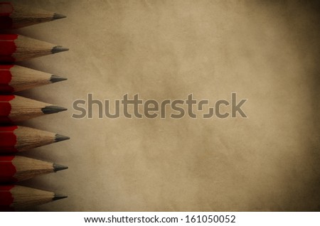 A column of pencil tips pointing inward, forming a border on the left side of a piece of parchment paper copy space with vignette.  Vintage style image for education or arts background.