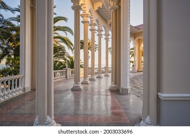 Columns and marble floor of the Ghagra Colonnade at sunset. The historical architectural structure opens the scenic view of the Black Sea and its coast with palms. Landscapes, travel, tourism.