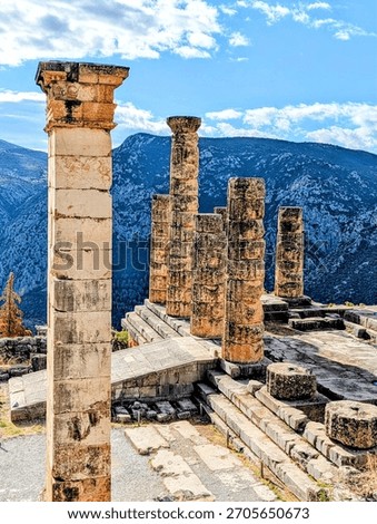 Columns of the Temple of Apollo in Delphi Greece with mountains in the background and a blue cloud filled sky above.