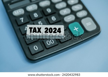 A colured wooden block with word “TAX 2024” in it sitting on top of calculator