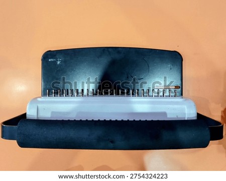 A comb binding machine with a black handle and white base, designed for office use.