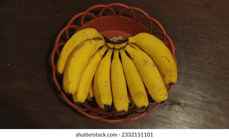 A comb of yellow ripe bananas on a woven bamboo basket with a wooden background ready to eat is good for body health - Powered by Shutterstock