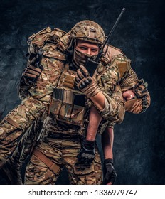 Combat conflict, special mission, retreat. Soldier special forces rescue his wounded teammate carrying him on his shoulders from the battlefield, talking on the radio and calls for support