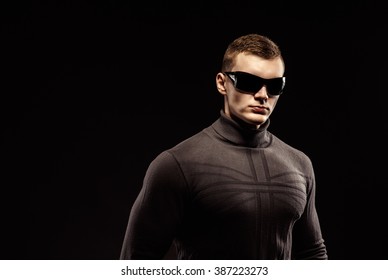 Combat muscled action hero man wearing brown sweater and sunglasses. Studio shot.