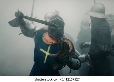 Combat squad of medieval knights of the Crusaders are in armors and helmets during the battle with swords in misty morning.