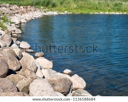 The combination of a beautiful summer blue sky, clear water, high green grass, and breeze-rippled waters create a striated, saturated and colored pattern of lines on an inland lake.  