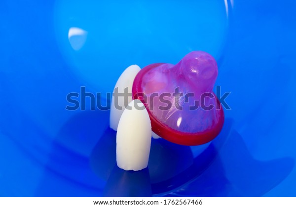Combination of chemical and mechanical barrier\
contraceptive methods. Spermicides in suppository form and red\
condom on blue\
background