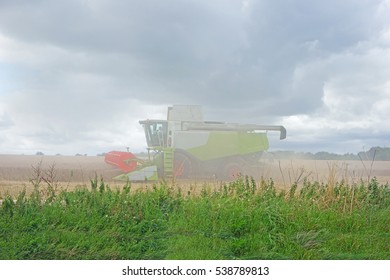 A Combine Harvester Cutting A Field Of Barley And Illustrating The Dusting Working Conditions Of Farm Workers, The Cotswolds, Gloucestershire, England, UK
