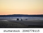 Combine harvester and tractor harvesting grains late at night in mist covered fields in the farmland of meteor impact crater Söderfjärden in Korsholm or Vaasa, in the region of Ostrobothnia, Finland.