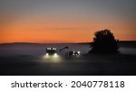 Combine harvester and tractor harvesting grains late at night in mist covered fields in the farmland of meteor impact crater Söderfjärden in Korsholm or Vaasa, in the region of Ostrobothnia, Finland.