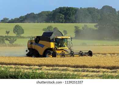 Combine Harvester Working At Harvest Time On Cotswold Farmland. England. UK