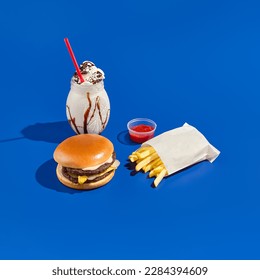 Combo meal with burger, fries, sauce, and milkshake on a blue background. Minimalist fast food photography featuring hard shadows, a bright blue backdrop, and a modern style