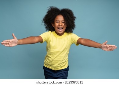 Come here, free hugs. Portrait of lovely good-natured little girl with curly hair in yellow T-shirt smiling excitedly and holding hands wide open to embrace, greeting. 