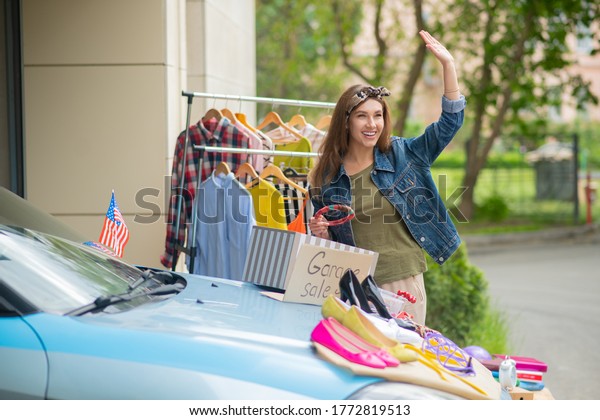 Come here. Nice positive\
woman waving with her hand while inviting her neighbors to the\
garage sale