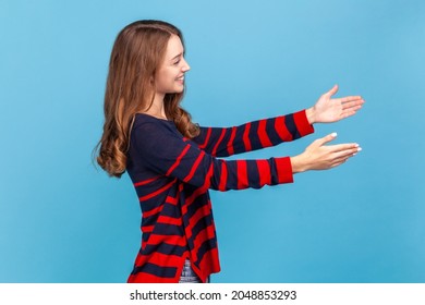 Come into my arms! Side view of friendly woman in sweater, giving free hugs with outstretched hands, welcoming inviting to embrace, support and care. Indoor studio shot isolated on blue background. - Shutterstock ID 2048853293