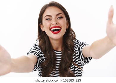 Come To Me. Cheerful Charming Friendly-looking Alluring Woman Reaching To Give Kiss, Stretch Hands Sideways Hold Camera, Taking Selfie Photographing In Glamour Outfit, Stand White Background