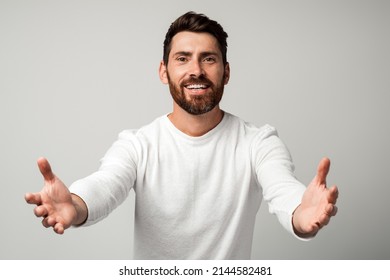 Come to me. Portrait of friendly kind man in casual white shirt holding arms wide open for free hugs and smiling happily, welcoming, going to embrace. indoor studio shot isolated on grey background 