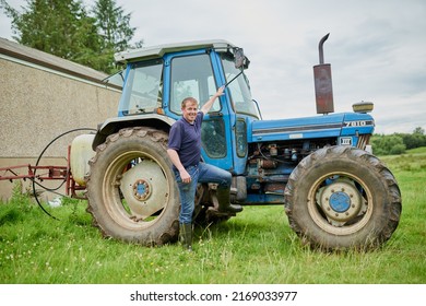 Come Take A Look In My Office. Portrait Of A Cheerful Young Farmer Posing Next To His Large Farm Tractor Outside On A Field.