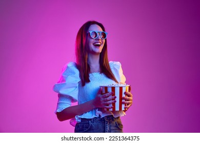 Comedy film. Portrait of young emotive girl posing in 3D glasses with popcorn basket over pink background in neon light. Concept of youth, beauty, fashion, lifestyle, emotions, facial expression. Ad - Powered by Shutterstock