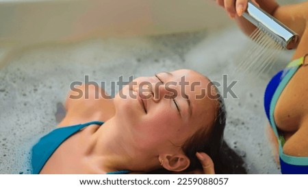 Comely mother and daughter take a bath with foam. Mom and small child body wash in bathtube. Mother takes care of her child. Concept hygiene, self care, healthy childhood, family health