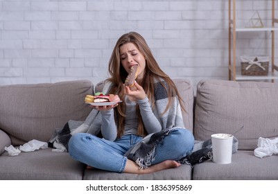 Comfort Foods And Stress Eating Concept. Frustrated Young Lady Devouring Pastry On Sofa At Home. Upset Woman Dealing With Negative Emotions, Anxiety Or Problems Through Sweets