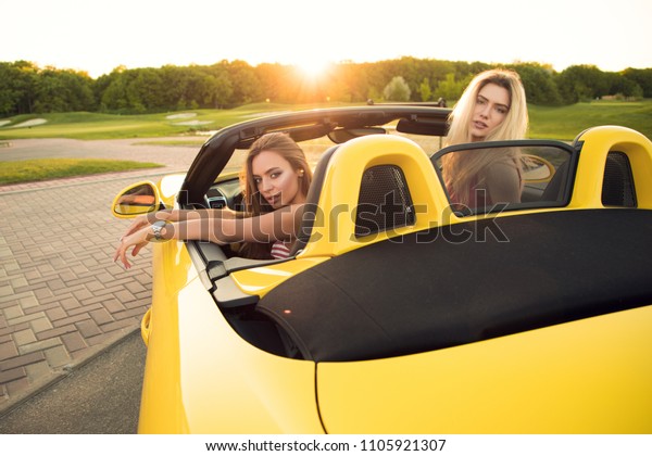 Comfort and luxury! Attractive gorgeous rich\
young flirting sexy girls sitting in the cabrio and looking behind,\
while posing at the camera.\
