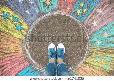 Comfort zone concept. Feet standing inside comfort zone circle surrounded by rainbow stripes painted with chalk on the asphalt.