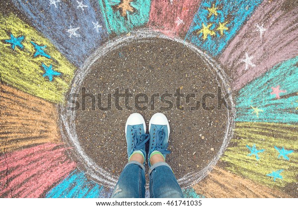 Comfort zone concept. Feet standing inside\
comfort zone circle surrounded by rainbow stripes painted with\
chalk on the asphalt.