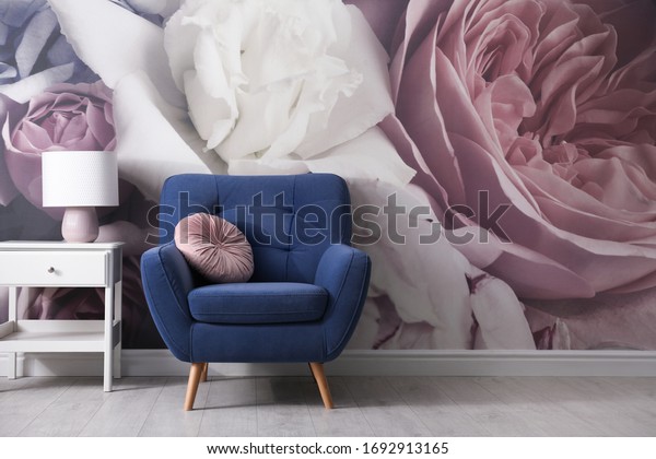 Comfortable armchair near wall with floral wallpaper. Stylish living room interior