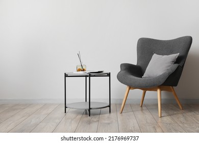 Comfortable Armchair With Table And Air Freshener Near Light Wall In Room