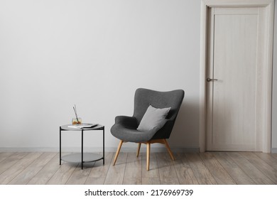 Comfortable Armchair With Table And Air Freshener Near Light Wall In Room