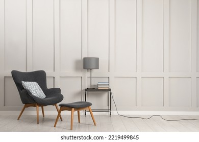 Comfortable armchair, table with lamp and books near light grey wall in room, space for text. Interior design - Shutterstock ID 2219499845