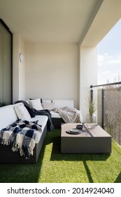 Comfortable balcony with fake grass and rattan corner sofa with pillows and square coffee table