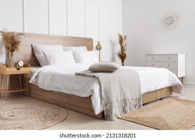 Comfortable bed, dry reeds and chest of drawers near white wall - Powered by Shutterstock